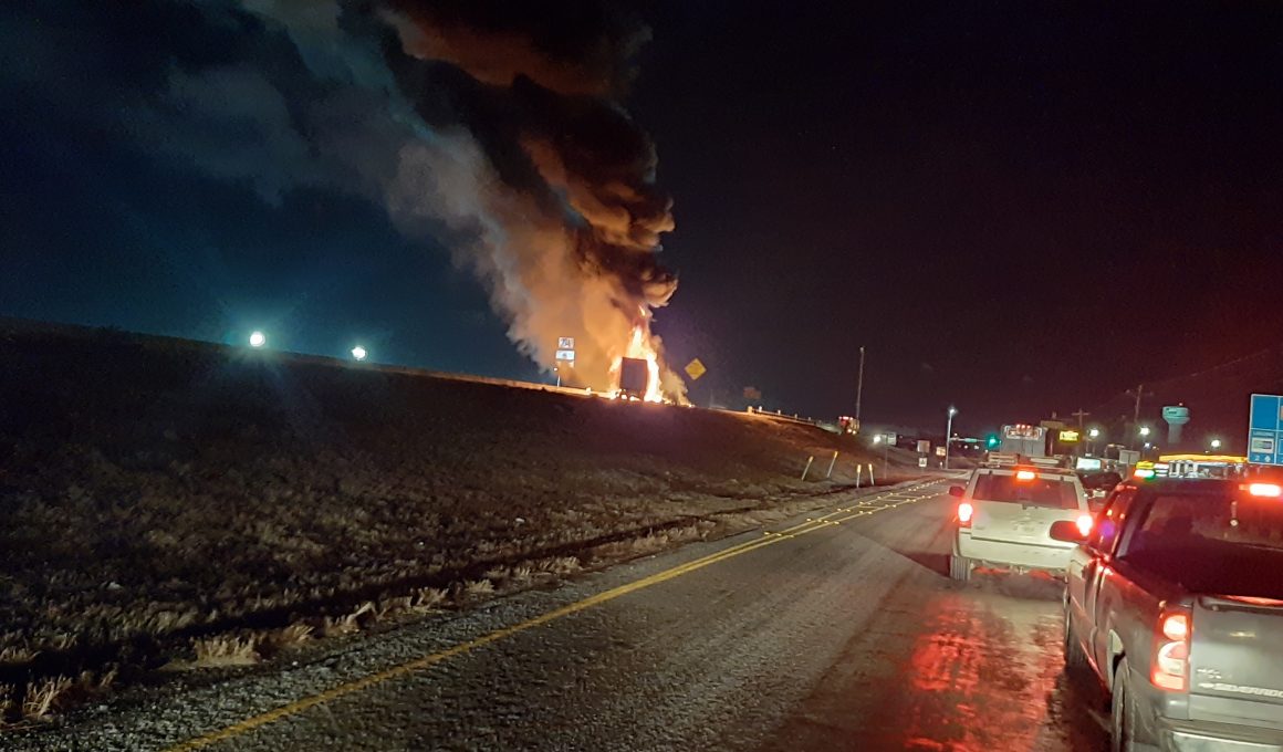 Image of a truck on fire in the median of a highway at night.