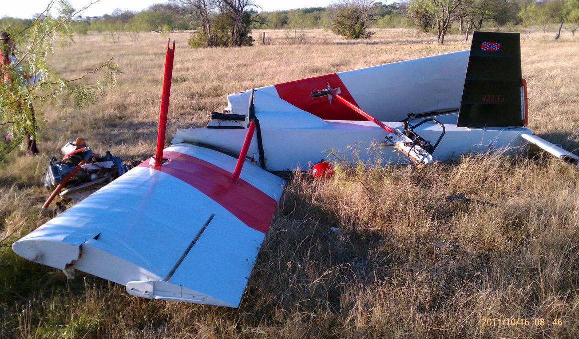 Image of small aircraft wreckage on grass. Confederate flag on the plane's vertical stabilizer.