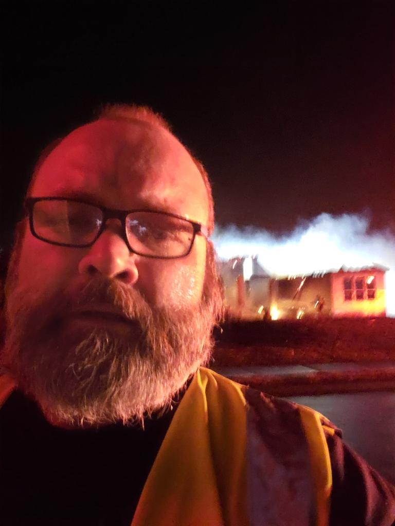 A paramedic's face with a house fire in the background at night