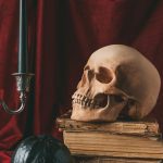 Halloween skull on ancient books with black pumpkin and candle on red cloth — Photo by KateNovikova