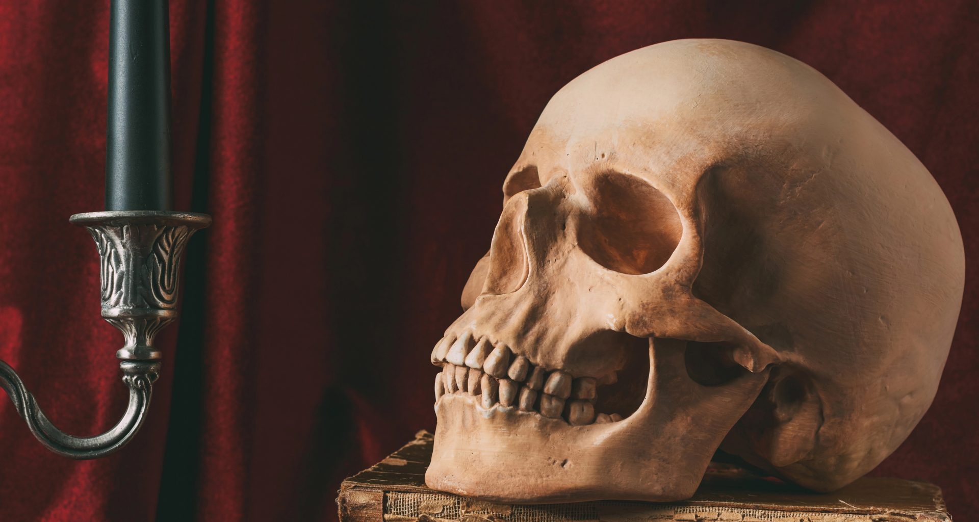 Halloween skull on ancient books with black pumpkin and candle on red cloth — Photo by KateNovikova