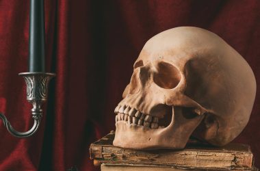 Halloween skull on ancient books with black pumpkin and candle on red cloth — Photo by KateNovikova