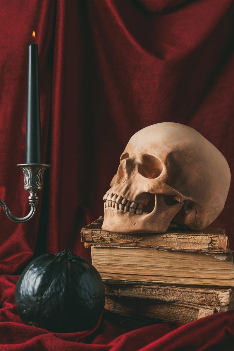Halloween skull on ancient books with black pumpkin and candle on red cloth — Photo by KateNovikova